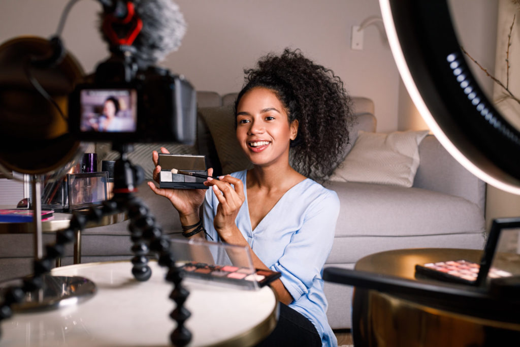 Eine junge Frau erstellt in ihrem Wohnzimmer Video-Content über Kosmetikartikel.