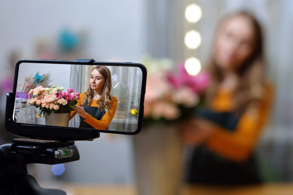 Die junge Besitzerin eines kleinen Blumenladens erstellt per Smartphone persönlichen Content für ihre Social-Media-Kanäle. 