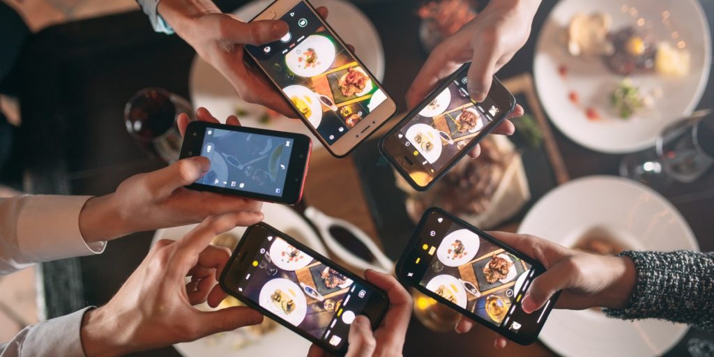 Mehrere Personen fotografieren das Essen in einem Restaurant und erstellen so User Generated Content für Social Media.